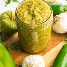 green enchilada sauce surrounded with peppers and garlic on cutting board