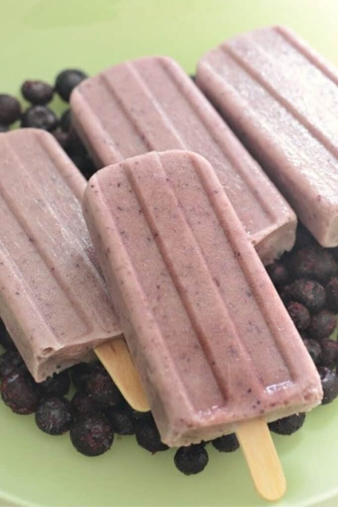 Four homemade blueberry popsicles on a green plate with whole blueberries