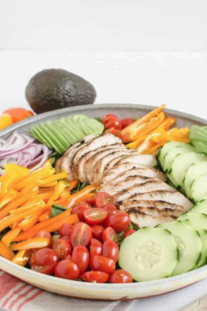 A large serving bowl of salad topped with a variety of colorful vegetables and sliced grilled chicken