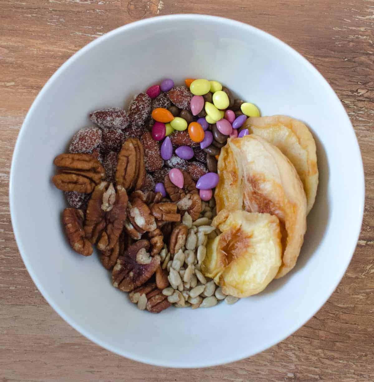 Trail Mix - Dried white peaches, honey torred almonds, pecans, sunflower seeds, and candy-coated sunflower seeds.pêssegos brancos secos, amêndoas torradas de mel, nozes, sementes de girassol e sementes de girassol revestidas de rebuçado.