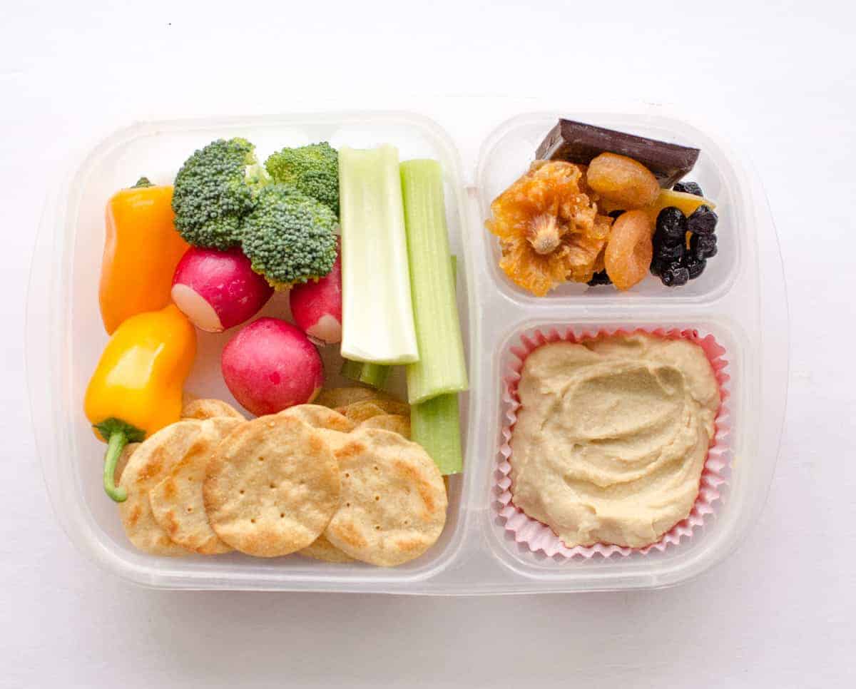 Clear plastic food container with different foods in each of the 3 spaces with fruits, vegetables, and other easy to eat foods.