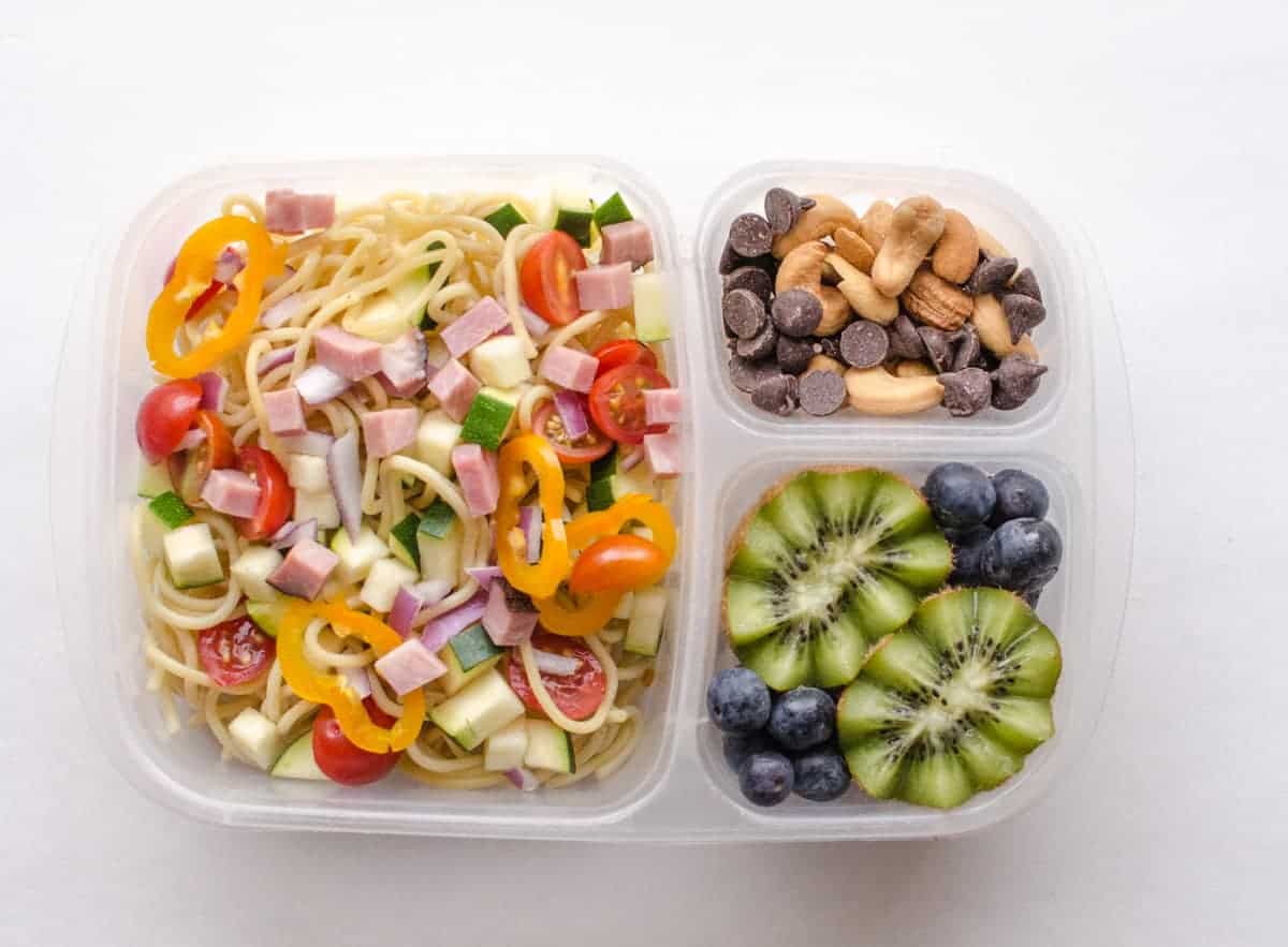 Clear plastic food container with different foods in each of the 3 spaces with fruits, vegetables, and other easy to eat foods.