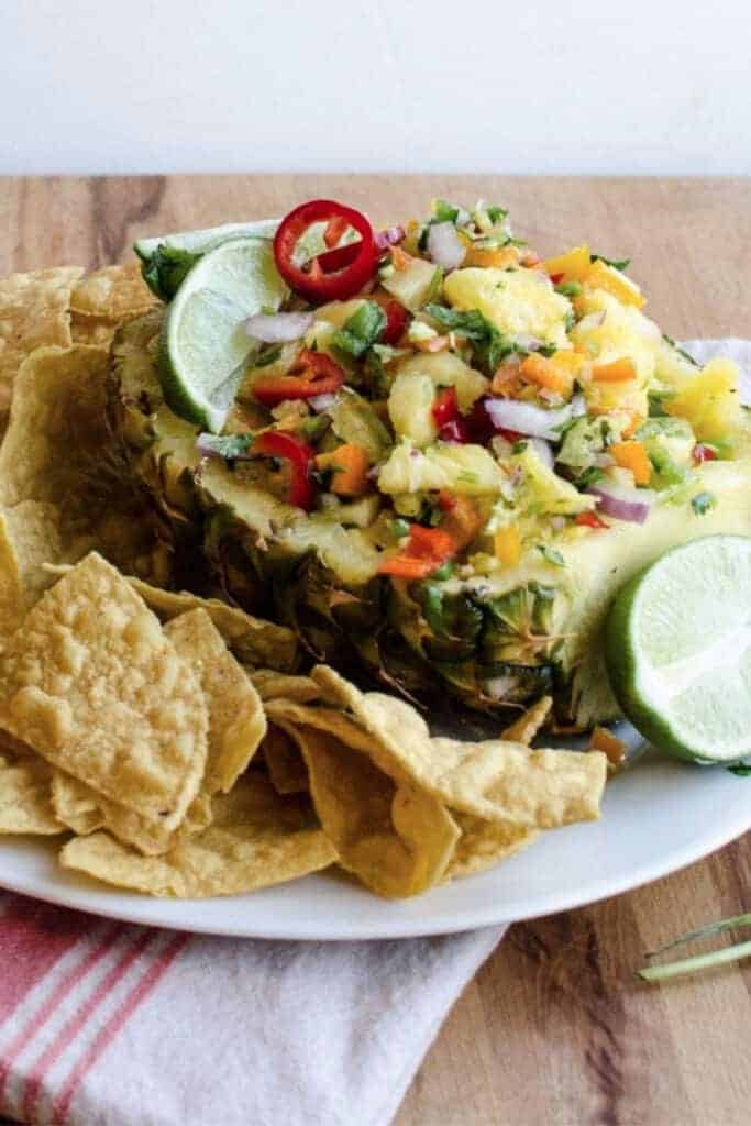side view of pineapple salsa and lime stacked into a pineapple rind with tortilla chips