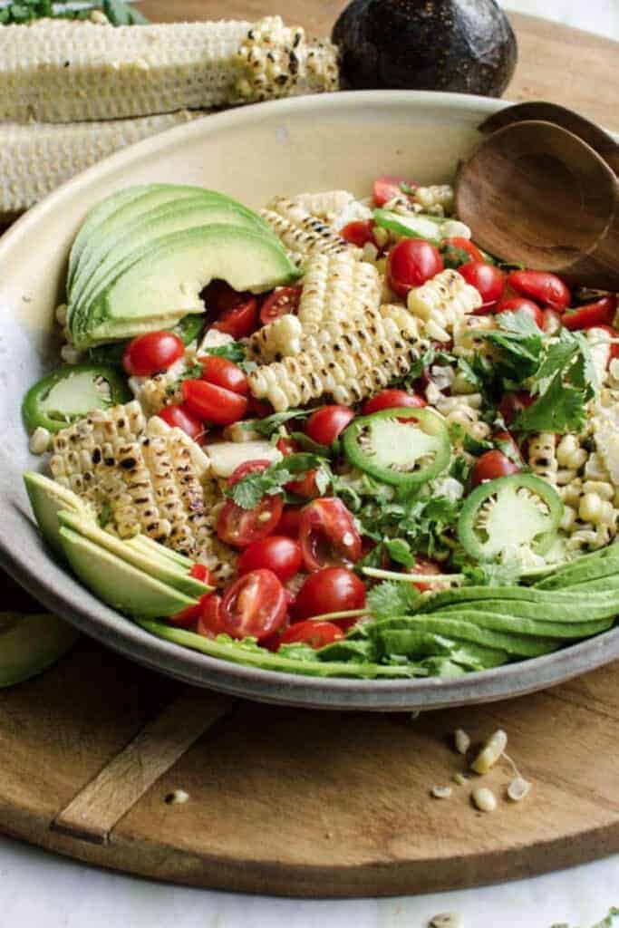 A large serving bowl of salad with sliced avocado, grilled corn kernels, grape tomatoes and sliced jalapenos
