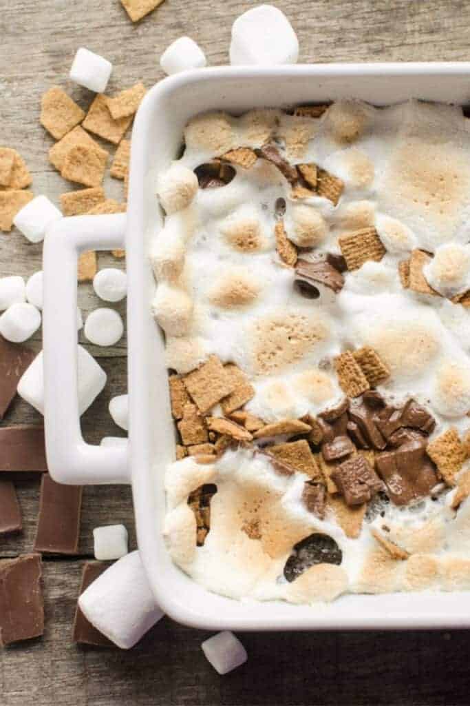 A baking pan of smores brownies with golden melted marshmallows, chocolate pieces, and graham cereal squares