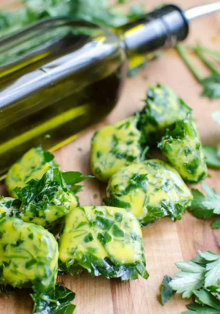 Herb bombs are a great way to save summer's herbs. Frozen herb bombs on a wooden cutting board with a bottle of olive oil in the background and some fresh herbs next to them.