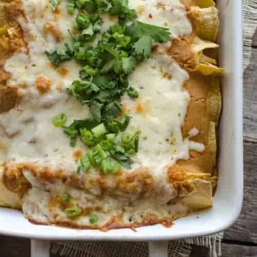 enchiladas in a white baking dish with pumpkin sauce and queso on top