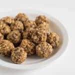 A white plate filled with round, homemade oatmeal energy bites made of oats, seeds, and nuts sits on a plain white background.