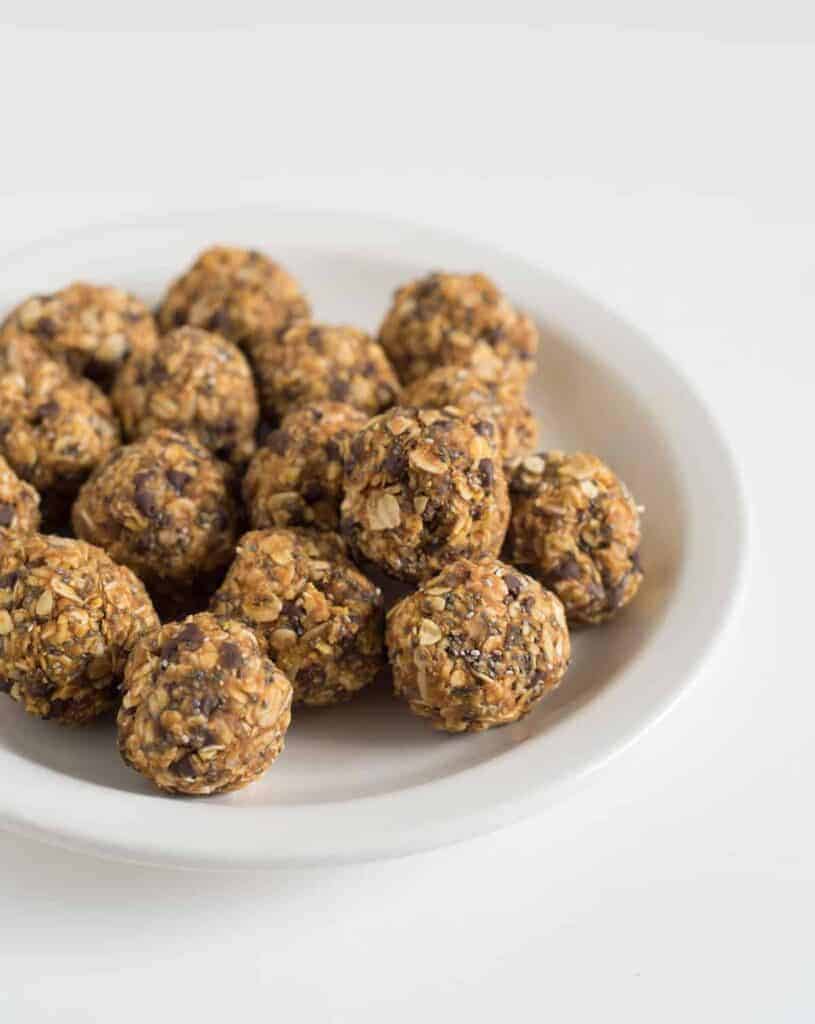 A white plate filled with round, homemade oatmeal energy bites made of oats, seeds, and nuts sits on a plain white background.