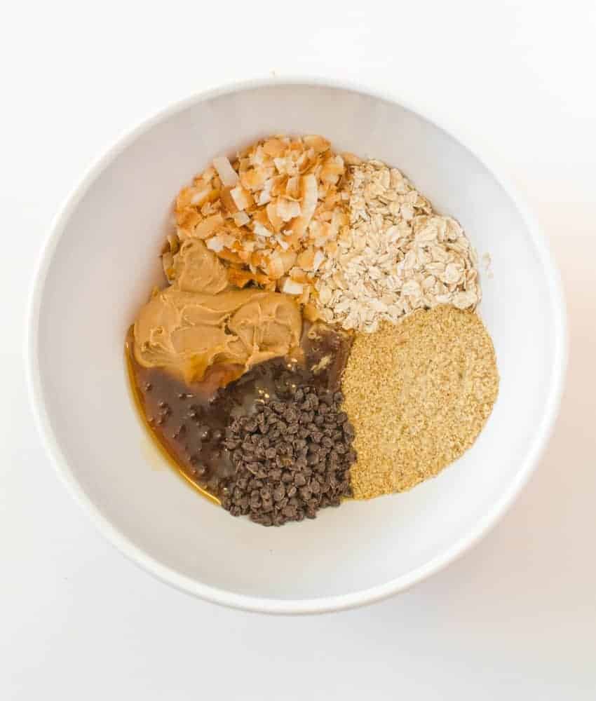 These Peanut Butter Chocolate Chip Oatmeal Energy Bites are perfect for snacks, dessert, lunch boxes, or post-workout recovery time. Ingredients for Peanut Butter Chocolate Chip Oatmeal Energy Balls including dry oats, peanut butter, honey, toasted coconut flakes, ground flaxseed, and mini chocolate chips.