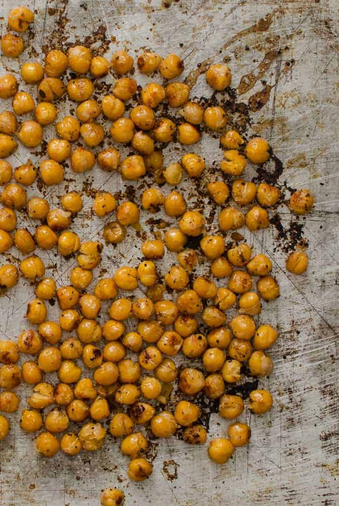 Easy Roasted Chickpeas are a great snack to eat right off the pan, or to store in the fridge as part of your weekly meal prep! Close-up of roasted chickpeas on a baking sheet.