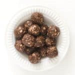 A white bowl filled with round, chocolate peanut butter bites mixed with oats rests on a white background, offering a delectable energy boost.