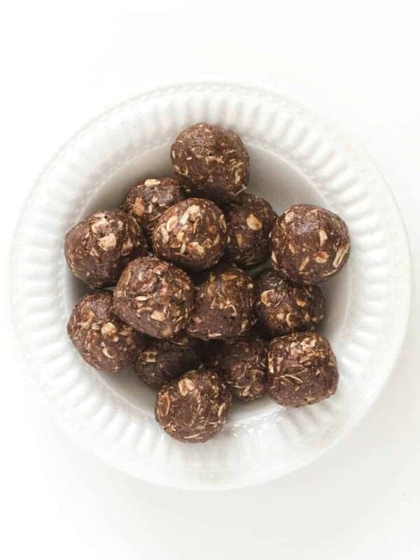 A white bowl filled with round, chocolate peanut butter bites mixed with oats rests on a white background, offering a delectable energy boost.