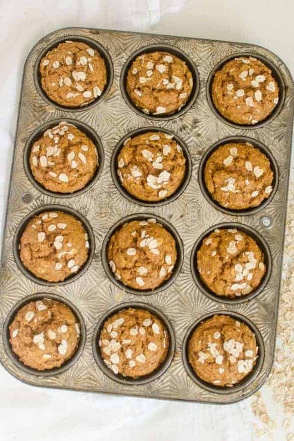 A dozen pumpkin muffins topped with oats in a muffin tins