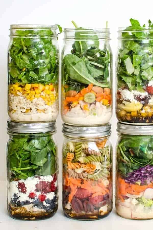 Six mason jars filled with different colorful layered salads