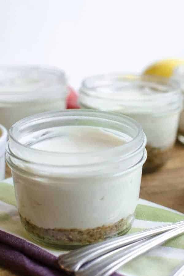 Small canning jars of healthy no-bake cheesecake on top of a crumbly crust layer