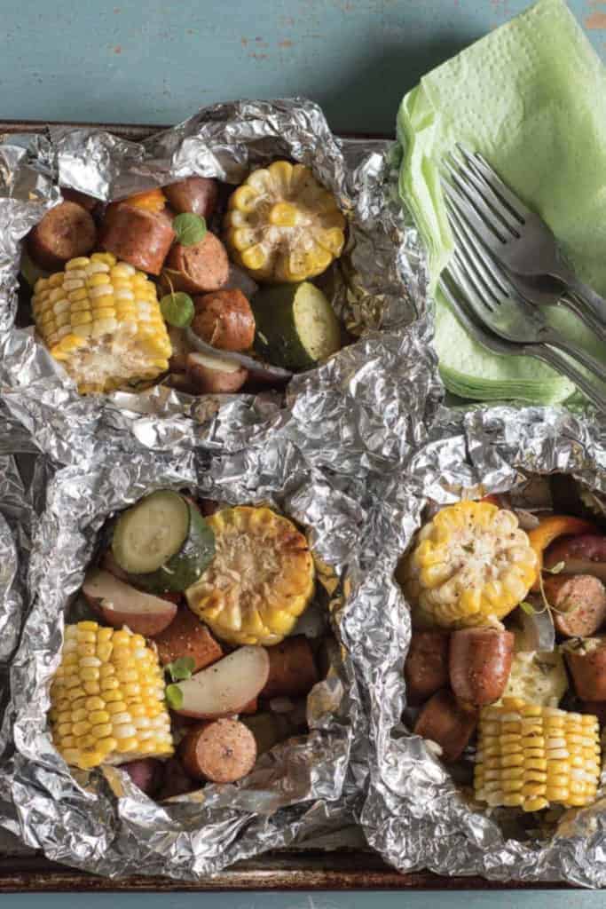Foil packets with chunks of sausage, potato, zucchini and corn on the cob