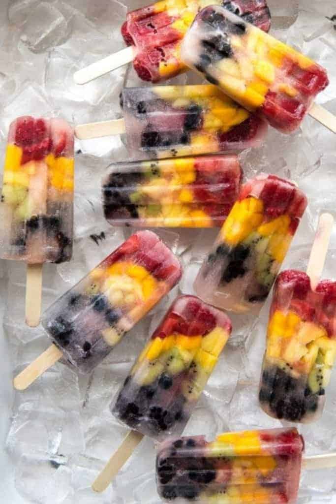 Homemade rainbow fruit popsicles in a tray of ice cubes