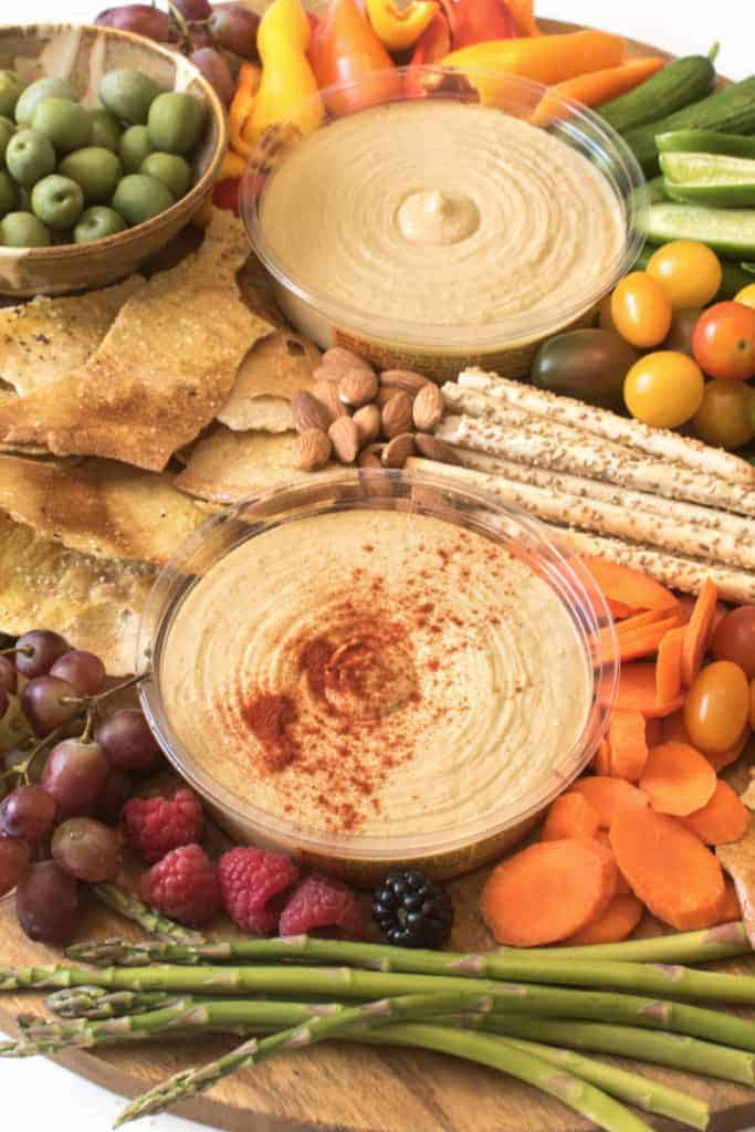 hummus dip with assorted cracker and nuts and olives and veggies on a platter