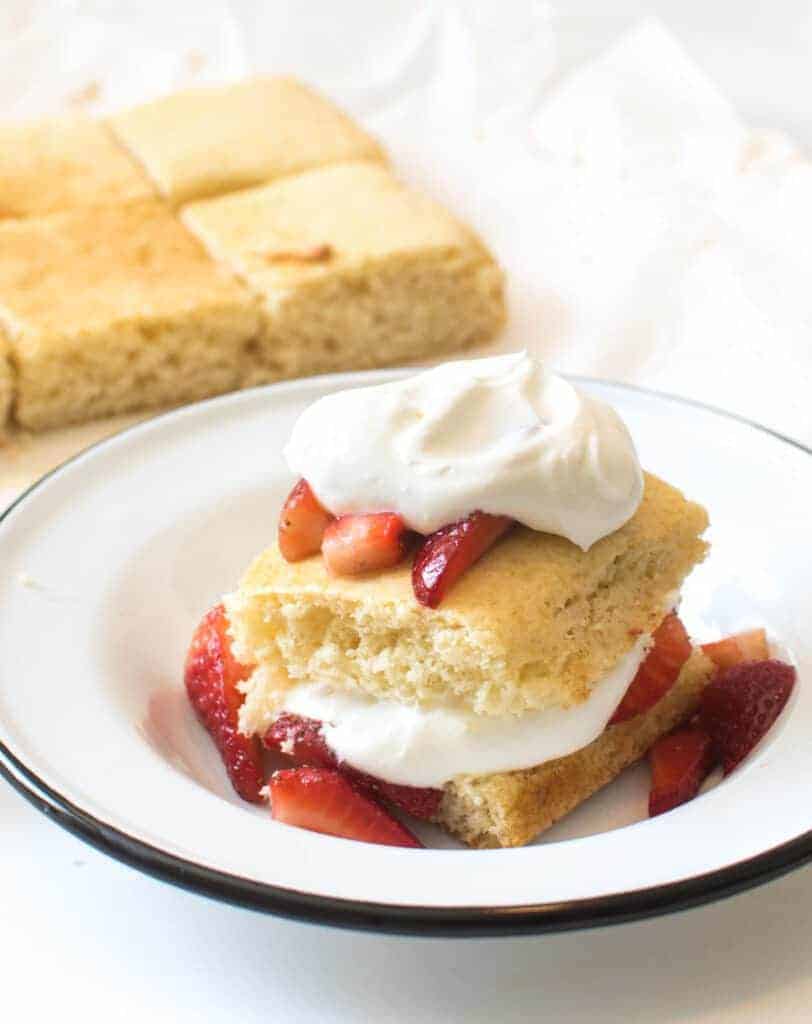 shortcake cut in halve and then layered with fresh strawberries and whipped cream in a white bowl