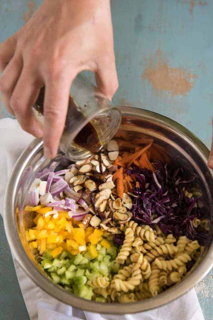 Dressing being poured over a mixing bowl of Asian Pasta Salad ingredients with colorful vegetables