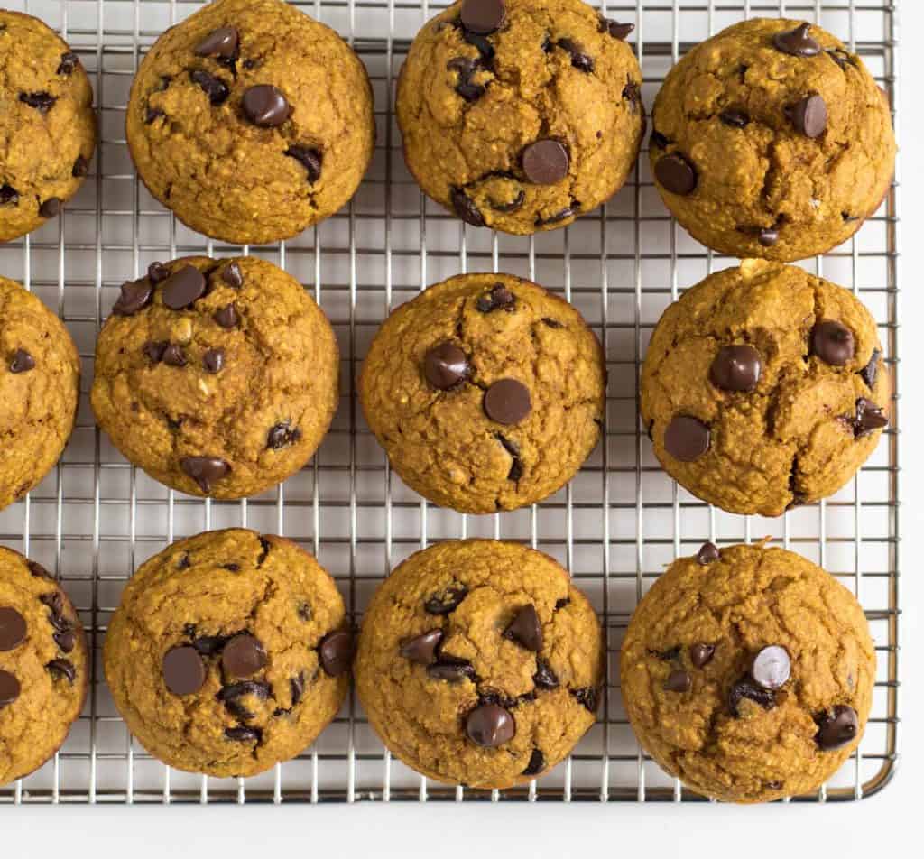 Twelve pumpkin chocolate chip cookies, reminiscent of Healthy Pumpkin Blender Muffins, are arranged in rows on a metal cooling rack. The cookies are round, golden-brown, and studded with chocolate chips.