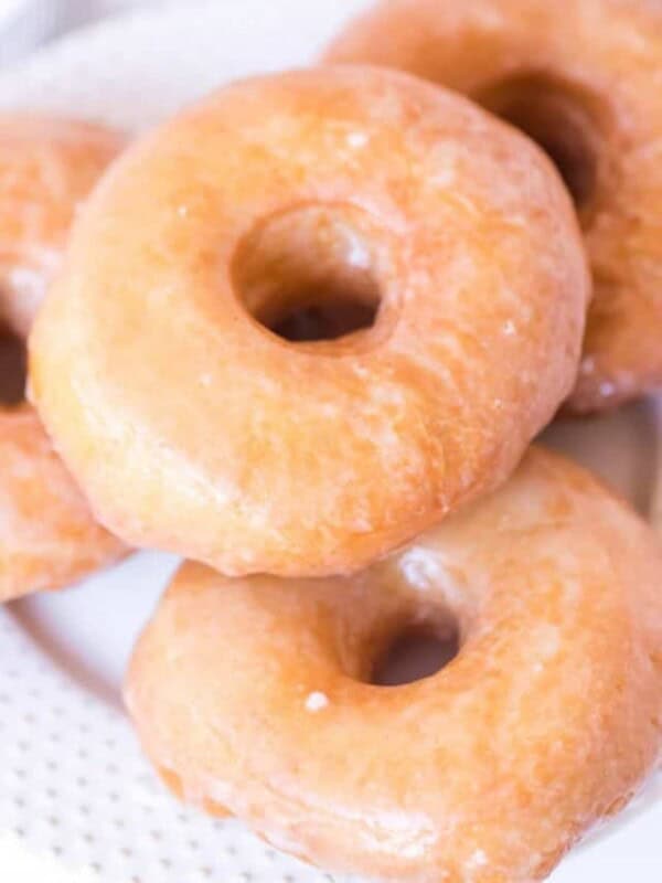 close up golden brown circle doughnut with shimmering glaze on white plate