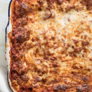 A close-up of a baked lasagna recipe in a rectangular dish, showing a golden-brown, bubbling cheese layer on top with slightly crispy edges.