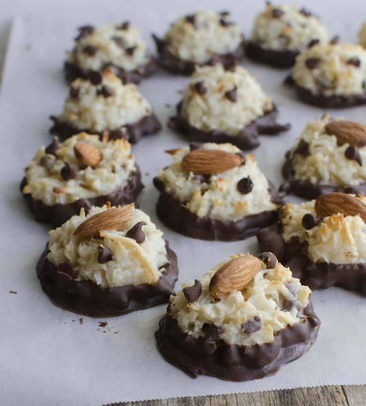 Close-up of a coconut macaroon with mini chocolate chips and a whole almond on top with the bottom of the cookie dipped in chocolate.