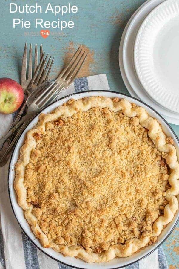 A Dutch apple pie with a crumbly topping sits on a blue surface. Nearby, an apple and several forks lay beside two stacked white plates. The text reads Delicious Dutch Apple Pie Recipe.