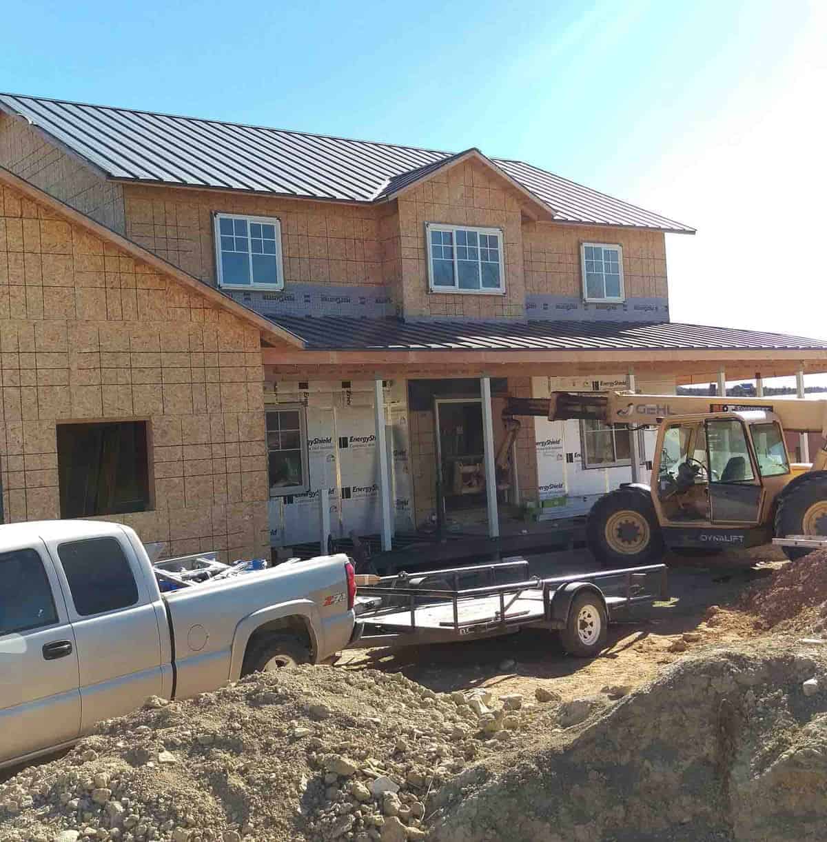 the exterior of the house with a tin roof on top. trucks are parked around it.