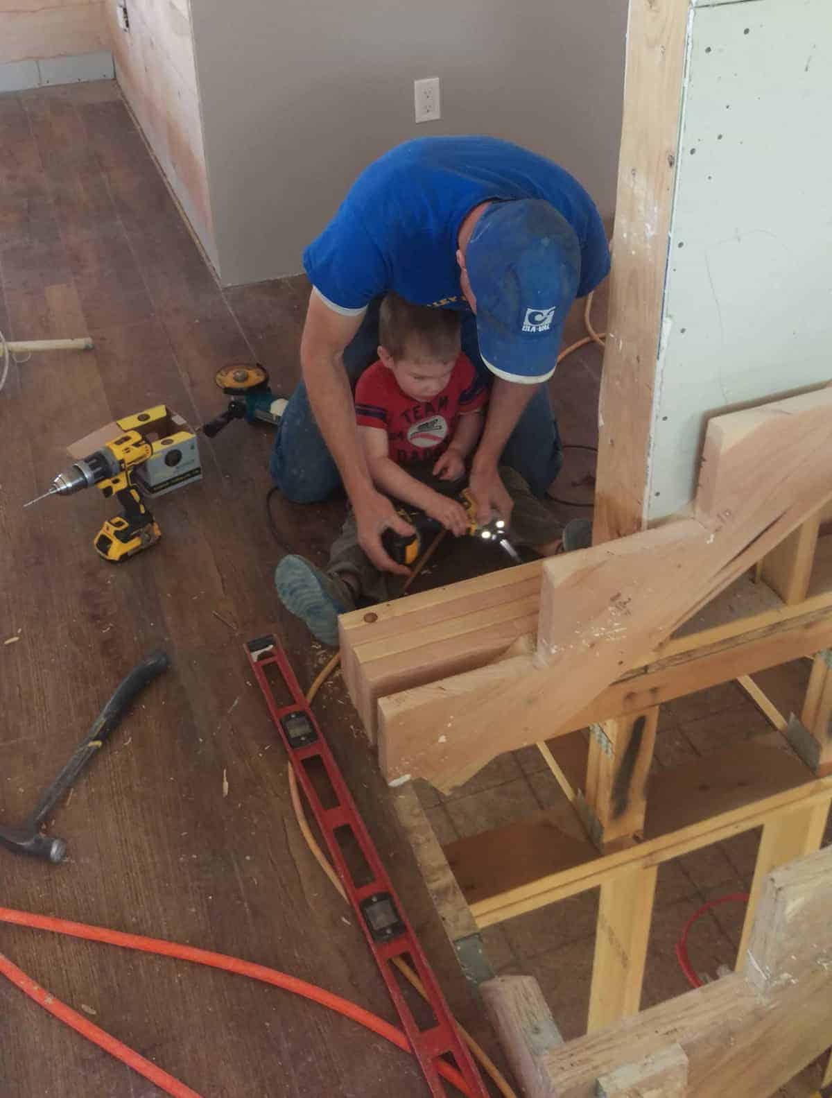 a man helping a toddler use a drill on a piece of wood