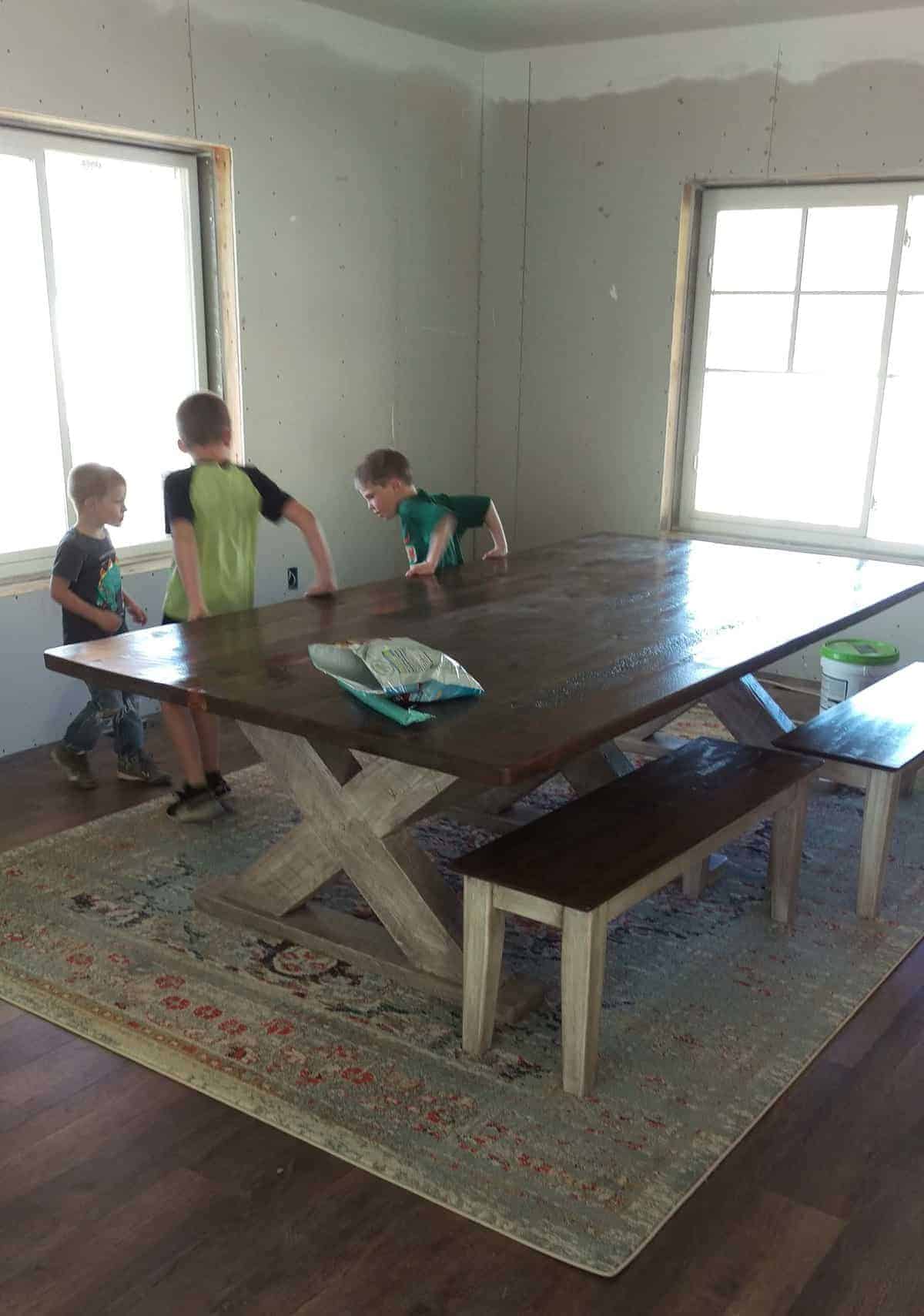 a large rug with a wooden table over it. three young boys play next to it.