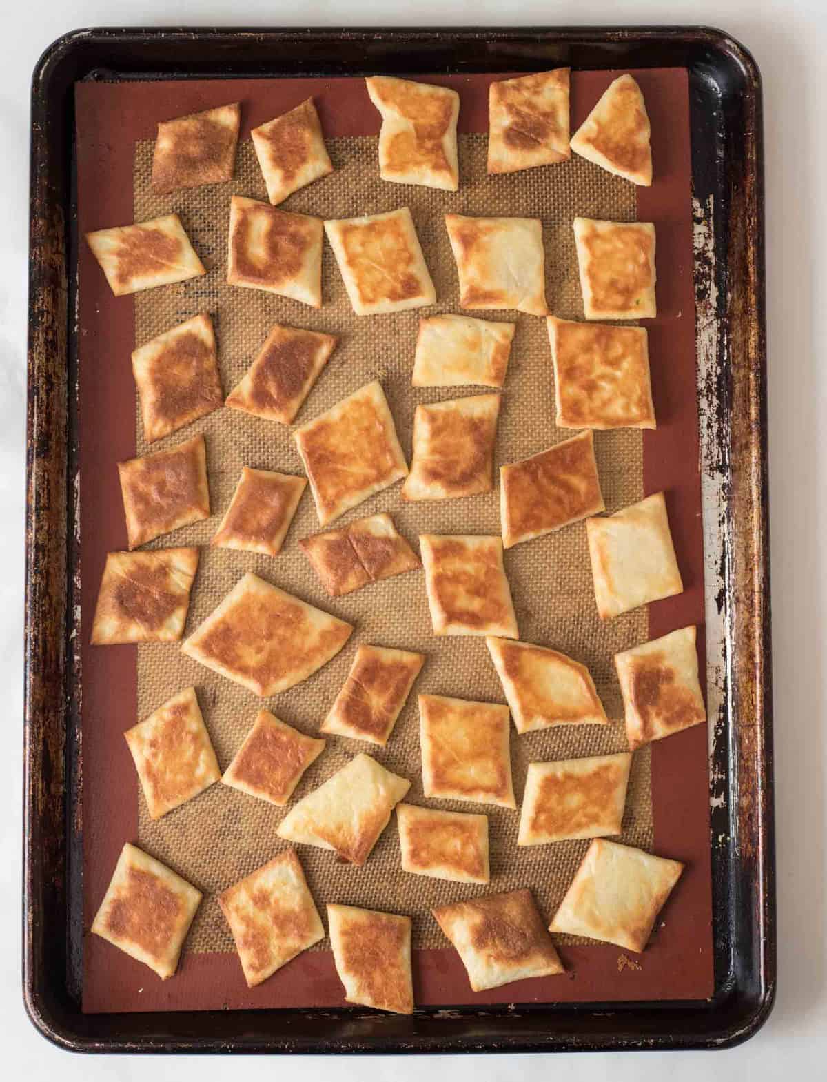 Baked flathead crackers on a silicone mat on a baking sheet.