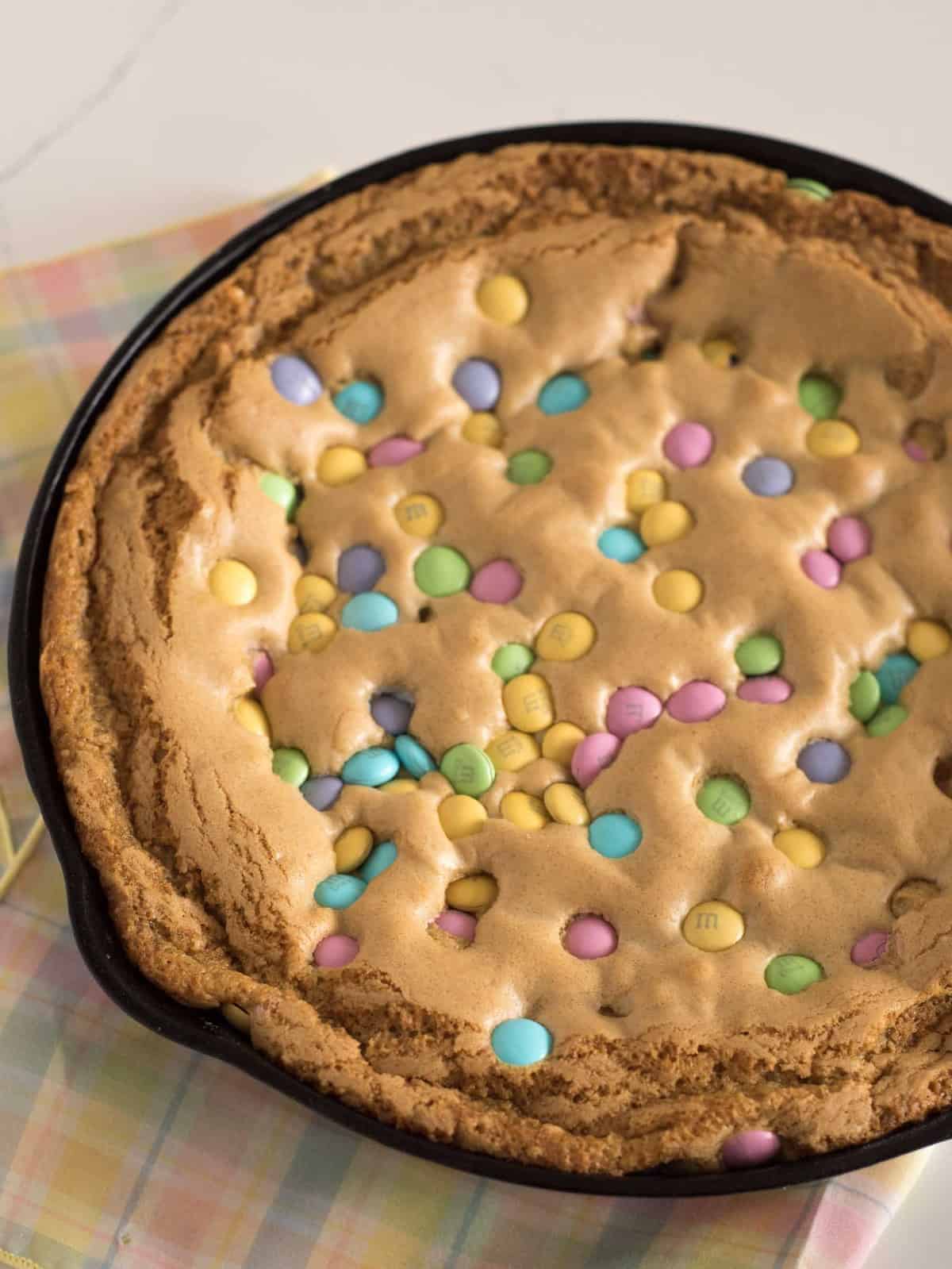 Cast iron skillet filled with a warm skillet cookies topped with pastel MandM candies