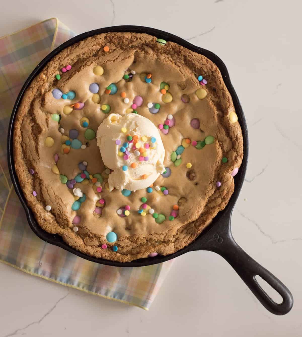 Easy skillet cookie recipe that is baked in a cast iron skillet topped with ice cream and sprinkles.