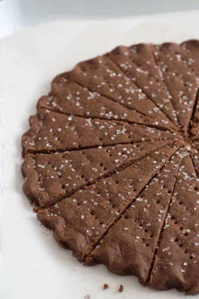 A round wheel of chocolate shortbread cookies with coarse sugar cut into wedges.