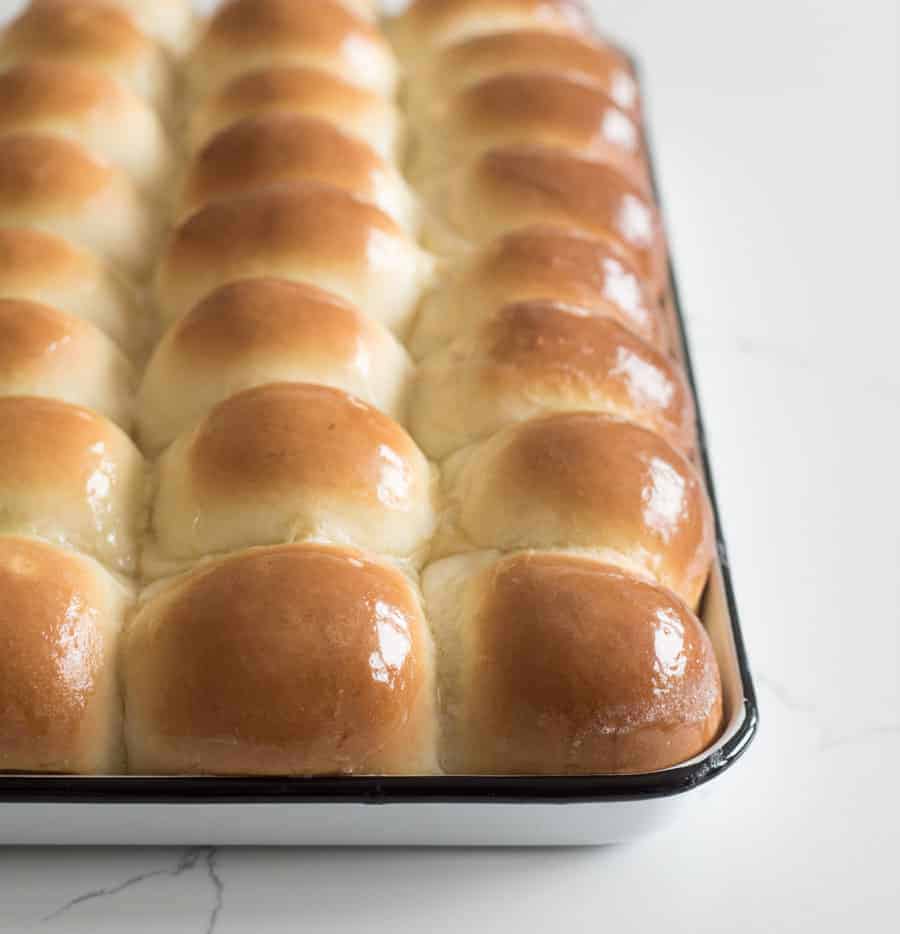 golden shiny dinner rolls hot out of the oven still in the pan with butter on top