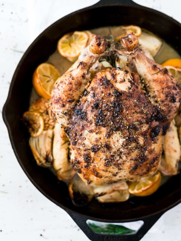 Image of a whole baked chicken in a pan with halved lemons