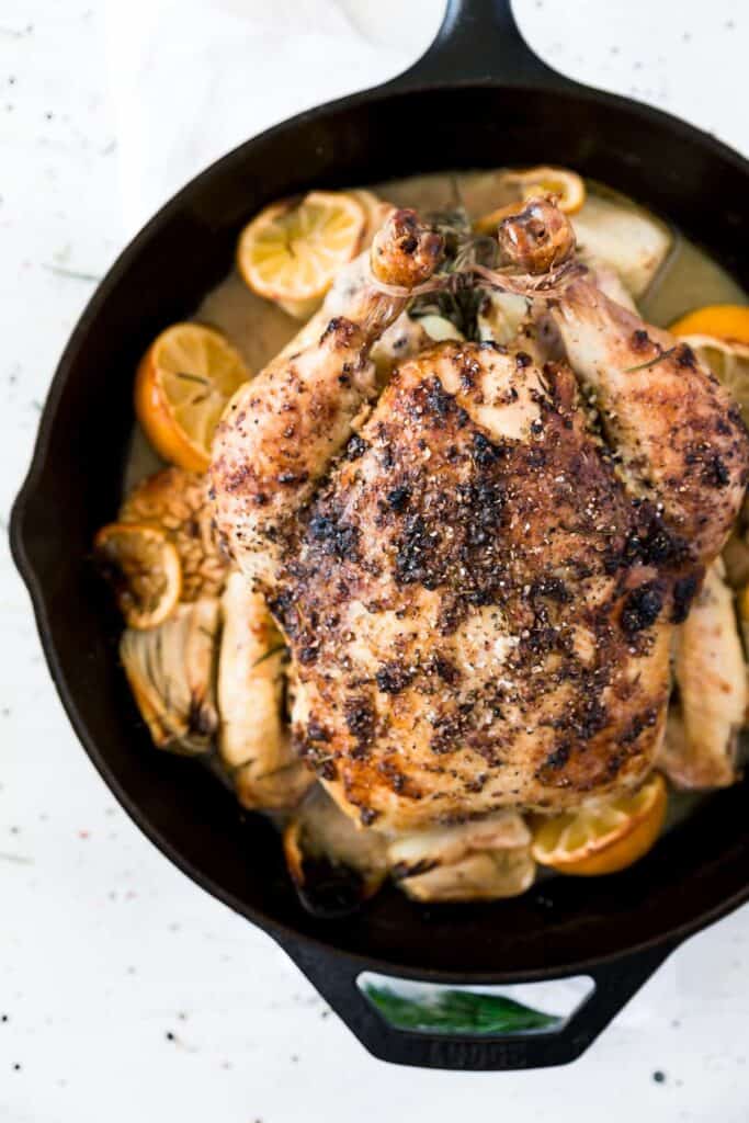 Image of a whole baked chicken in a pan with halved lemons