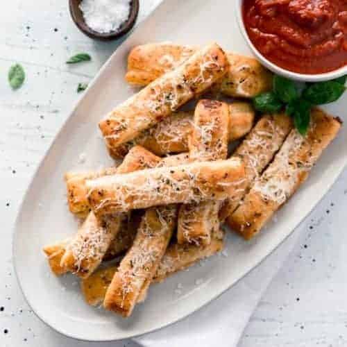 Plate of cheesy pizza sticks with cup of sauce