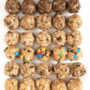 Rows of bite-sized no bake energy bites with various mix-ins, including chocolate chips, oats, and colorful candy pieces, arranged neatly on a white surface.