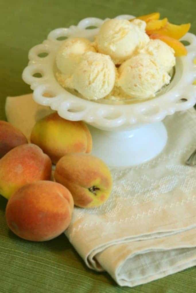 A few scoops of fresh peach ice cream with fresh peach slices in a decorative white dish