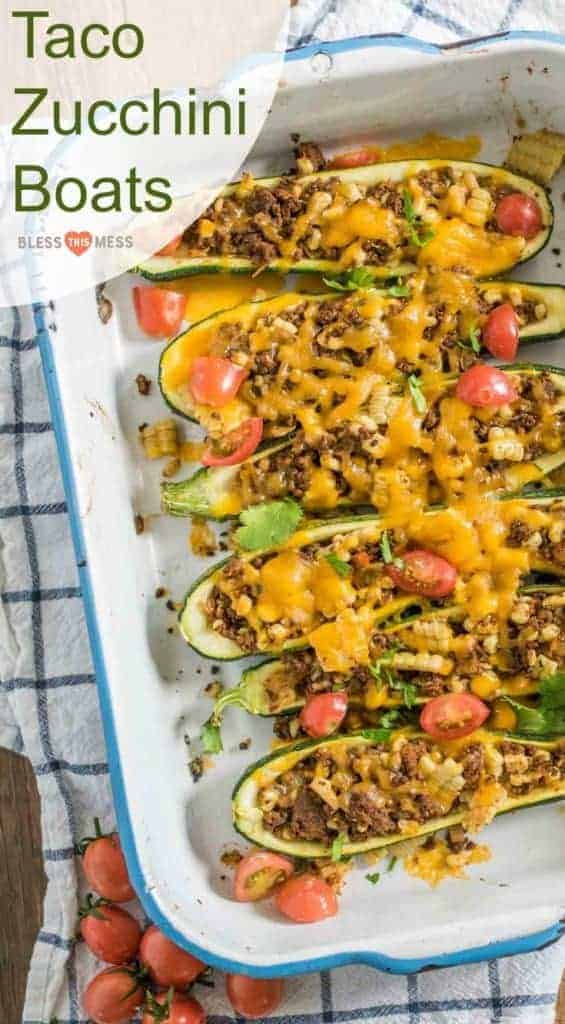 Zucchini halves in a baking dish filled with taco meat, melted cheese, and tomatoes