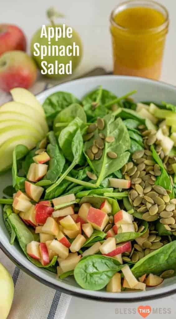 Title Image for Apple Spinach Salad and a large white bowl with baby spinach leaves, diced apple, and pumpkin seeds