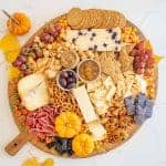 Top view of a round Halloween Cheese Board with crackers, pretzels, cheeses, meats, fall-colored candies, mini gourds