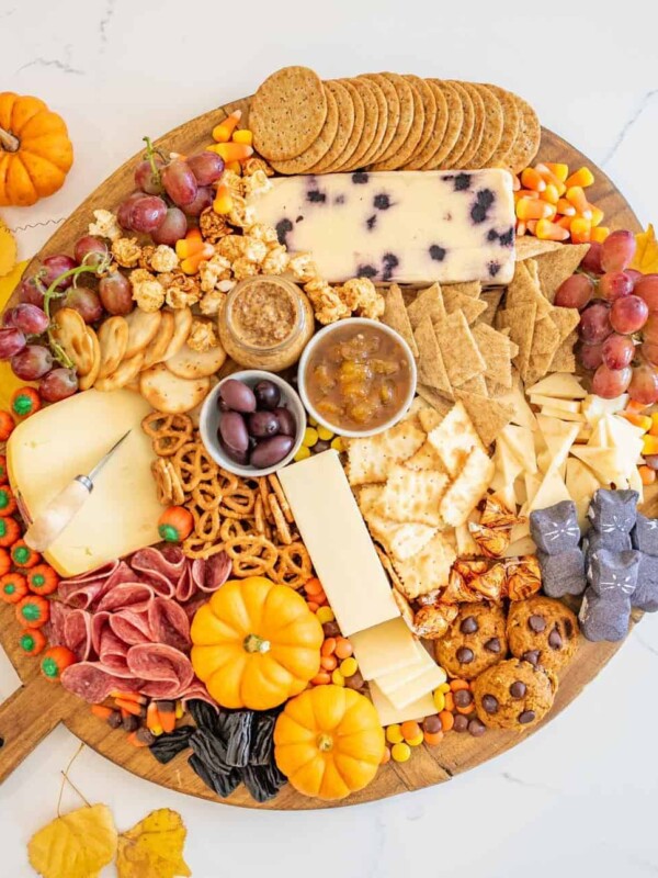 Top view of a round Halloween Cheese Board with crackers, pretzels, cheeses, meats, fall-colored candies, mini gourds