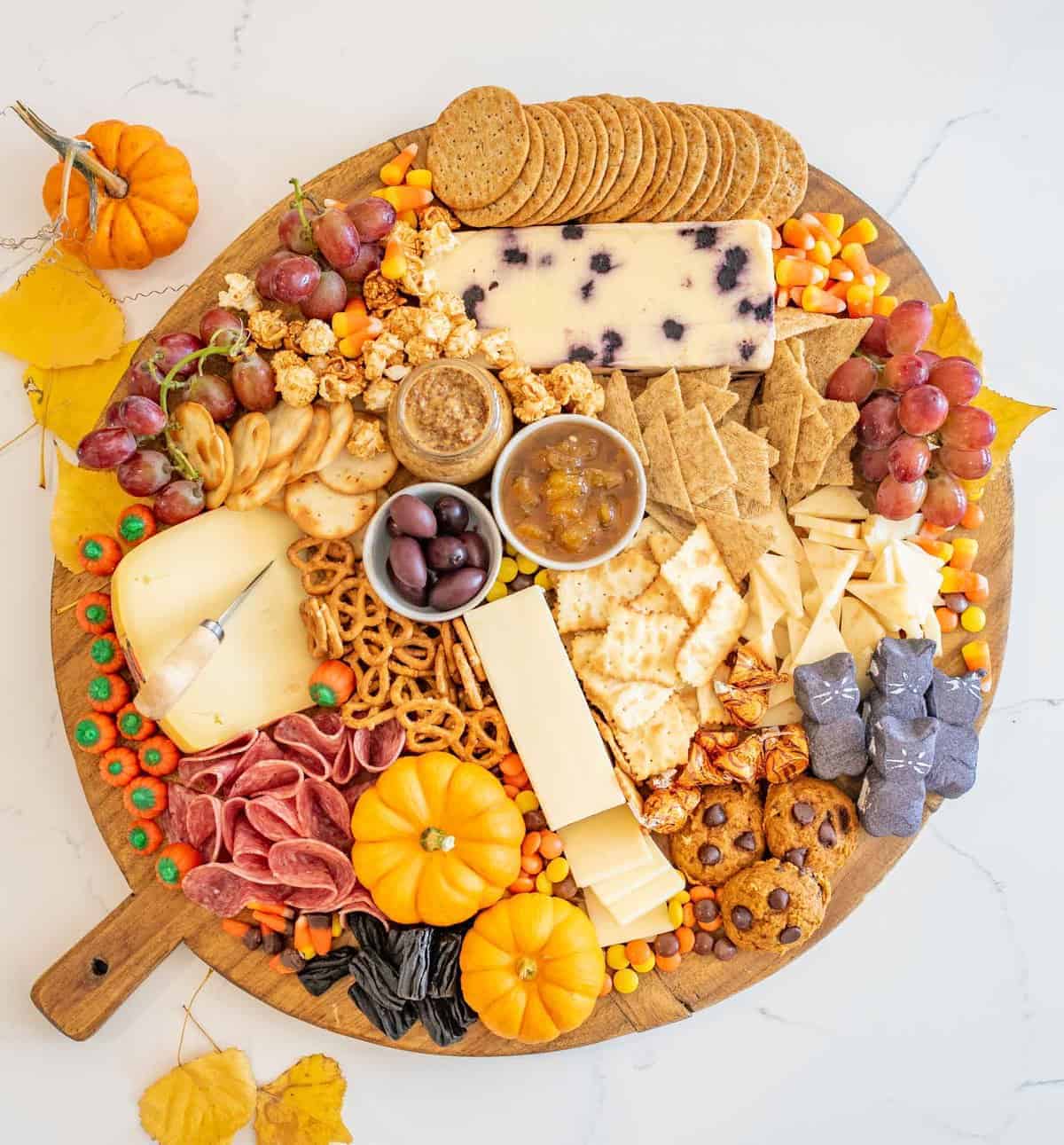 Top view of a round Halloween Cheese Board with crackers, pretzels, cheeses, meats, fall-colored candies, mini gourds