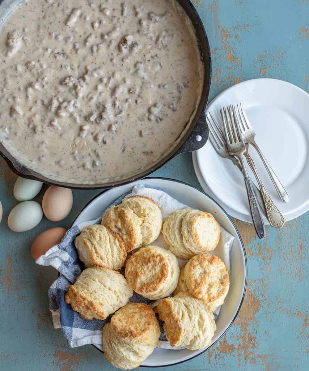 Cast iron skillet with sausage gravy in it and a white dish with fluffy biscuits in it ready to be served
