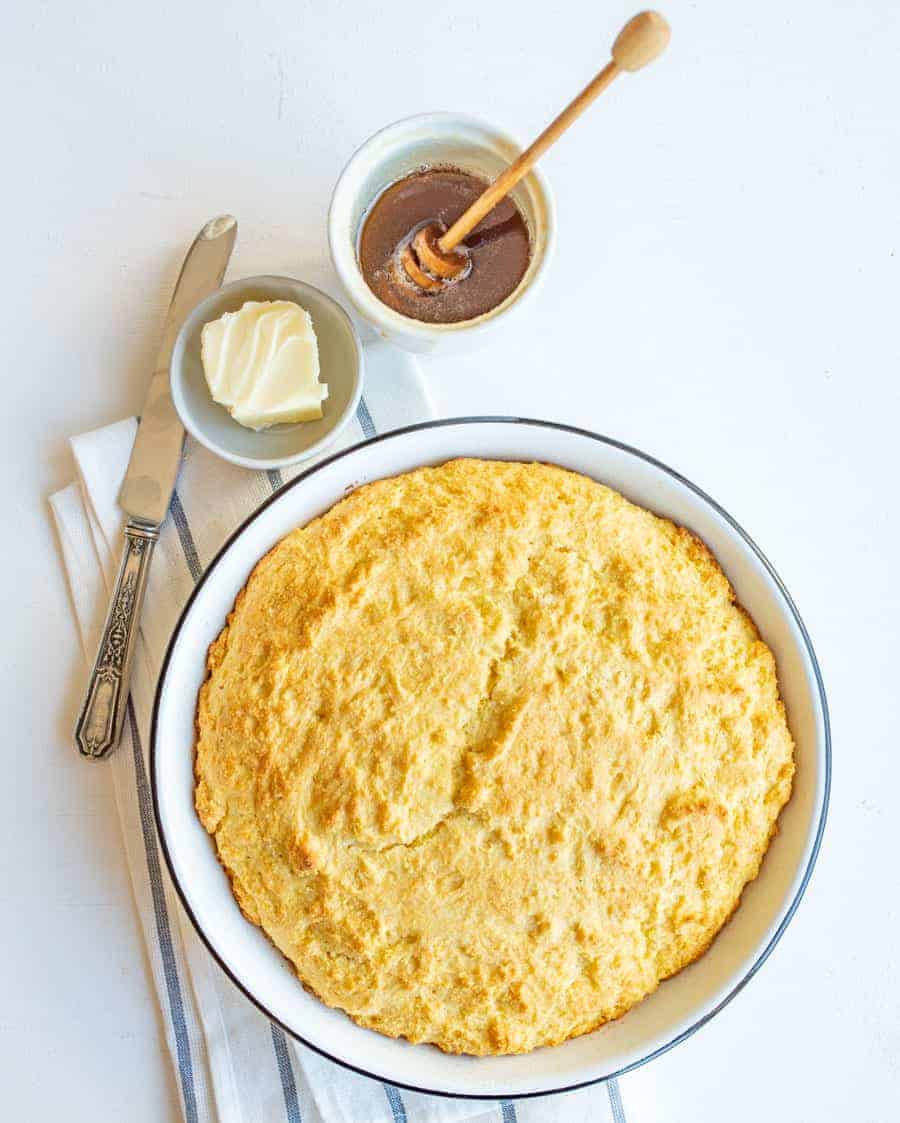 easy sour cream cornbread in round white dish with butter, honey, and butterknife